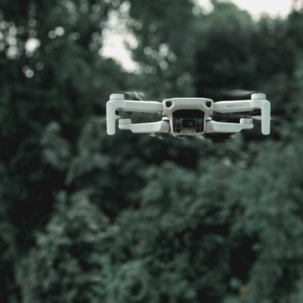 A white camera flying over trees with a forest in the background.